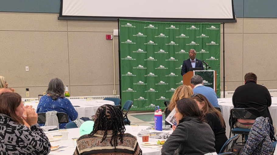 AFrican American man at a podium speaking before a large crowd