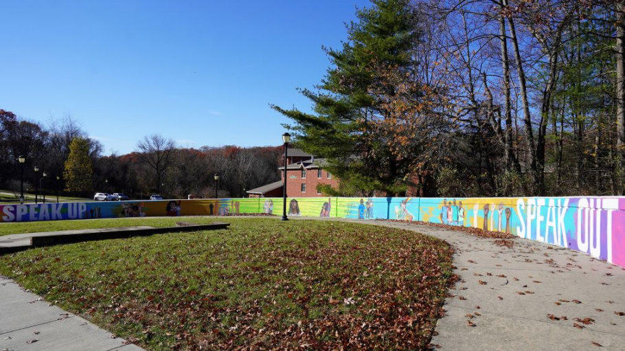 Wall featuring multicolored paintings of diverse young people and words including speak up and speak out
