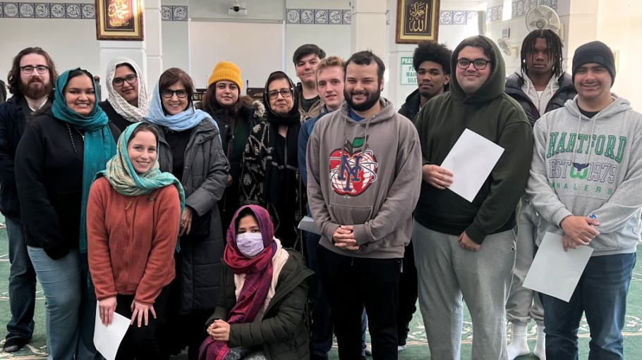 14 men and women of varied ages and races pose in a mosque prayer hall