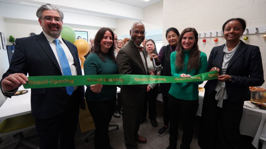 Six men and women in professional attire cut a large green ribbon