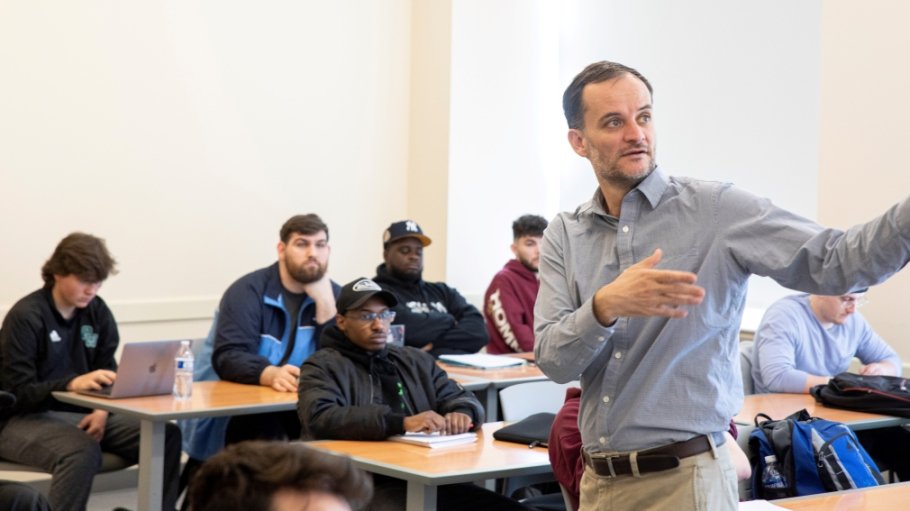 Male professor lecturing to class while turning towards a smartboard