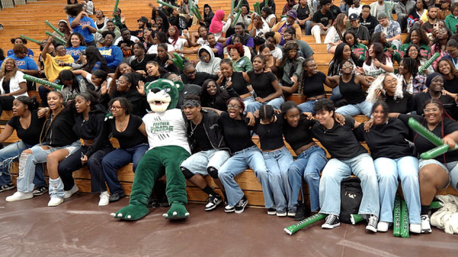 Large group of students sitting in bleachers with a green panther mascot