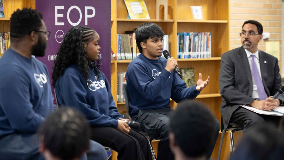 Hispanic young male speaks into a microphone as three others look on