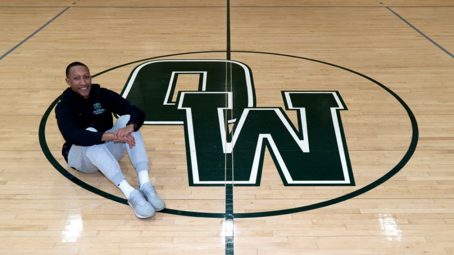 African American young man sits on a basketball court decorated by an OW logo
