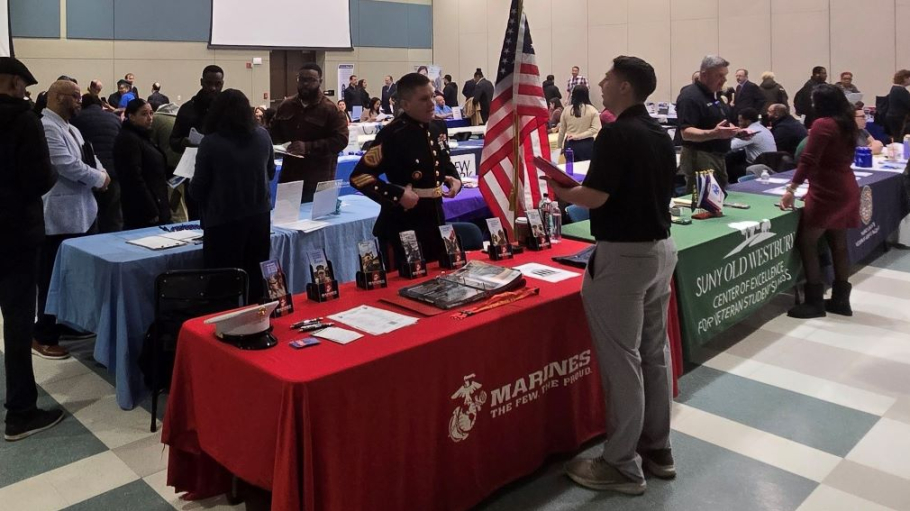 Large room set up trade show style with tables for organizations and students talking to representatives of those organizations 