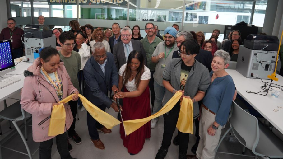 An African American man and a South Asian young woman hold a large pair of scissors above a recently cut ribbon as a crowd of 40 students and professors applaud