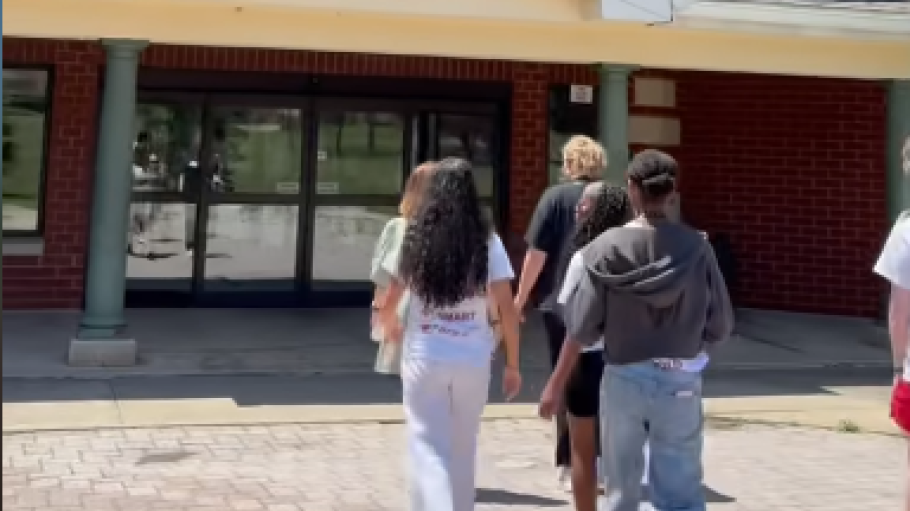 Students walk into a brick residence hall on a sunny day