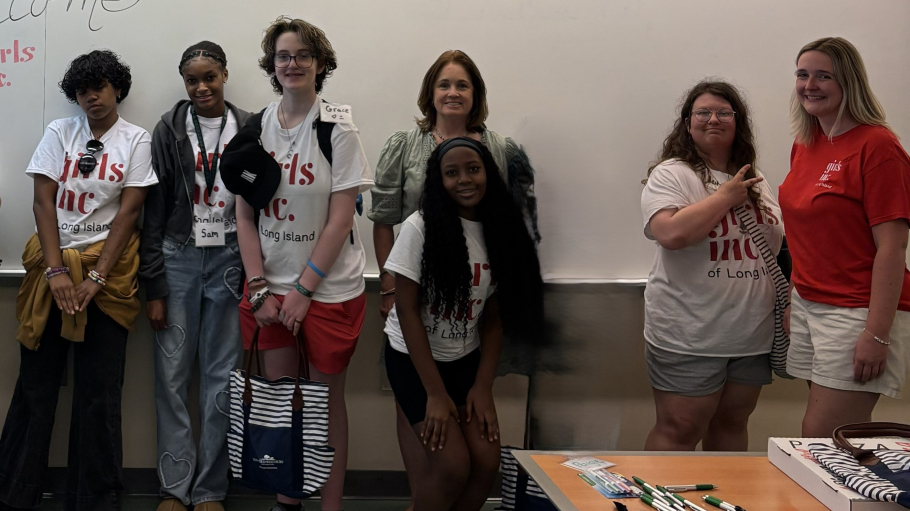 Six diverse young women pose in front of a classroom with a Caucasian woman in professional attire