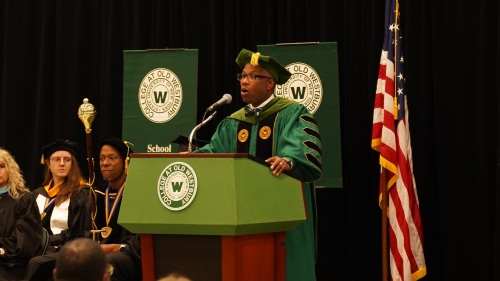 President Sams in academic regalia speaking from podium