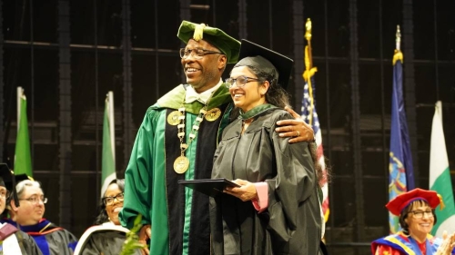 Campus president poses with a graduate with both wearing caps and gowns