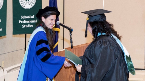 Female professor in blue regalia congratulates female student in black regalia