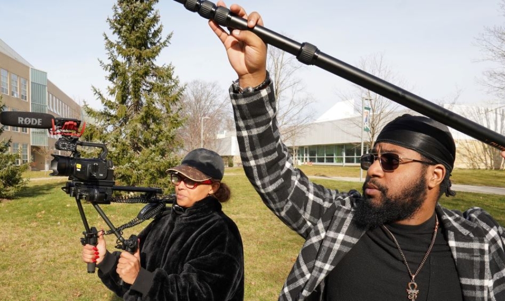 Two students working a camera and boom microphone