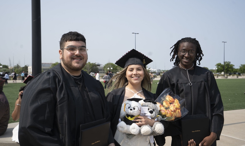 Three graduates pose outside the Nassau Coliseum