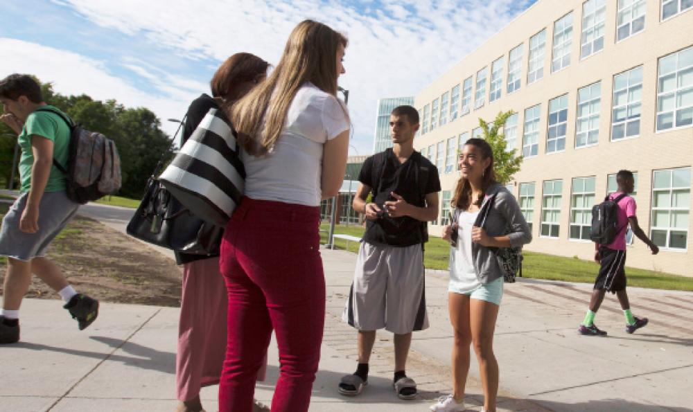 Diverse group of students walking on a college campus, carrying backpacks and chatting.