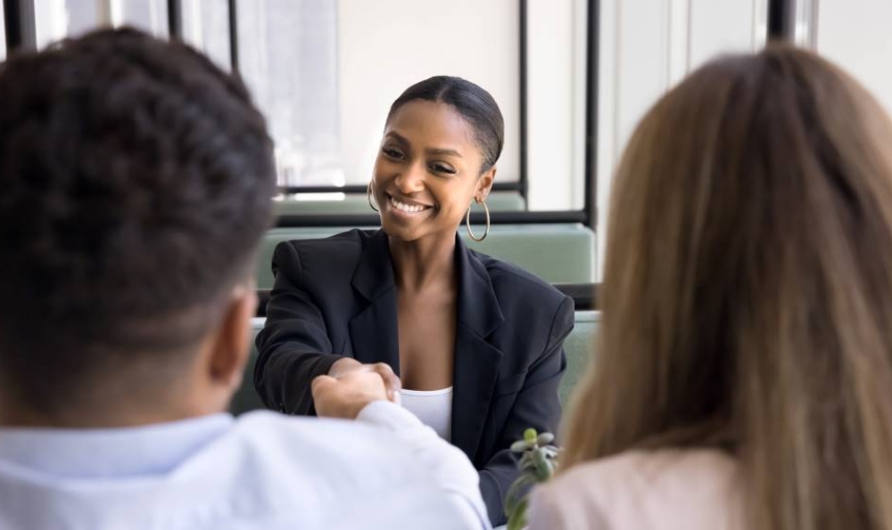 Positive confident African American woman in professional dress shaking hands with young couple of customers after giving consultation