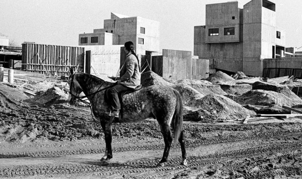 black-and-white photo of man on horseback looking at construction site