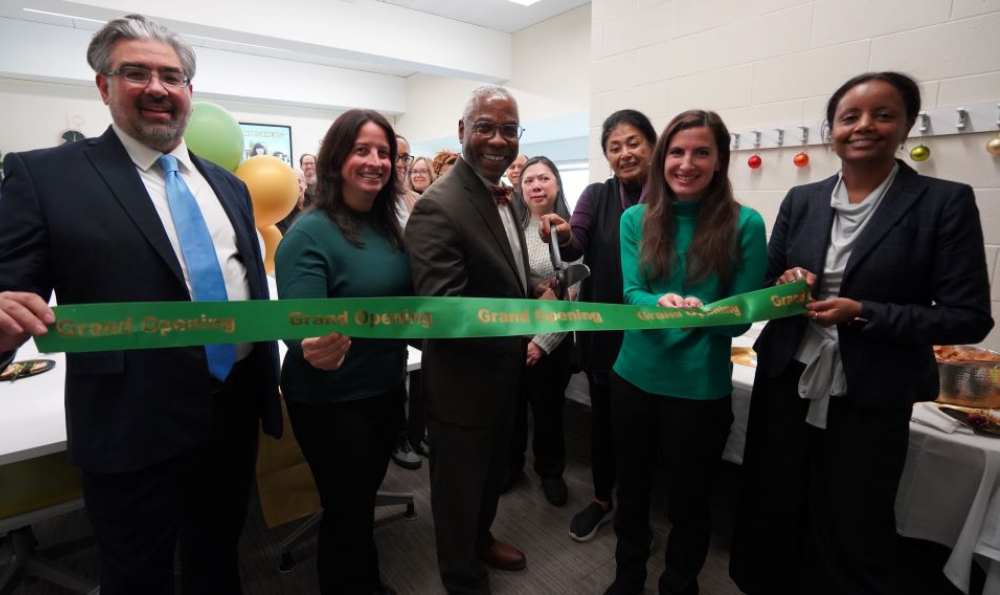 Six men and women in professional attire cut a large green ribbon