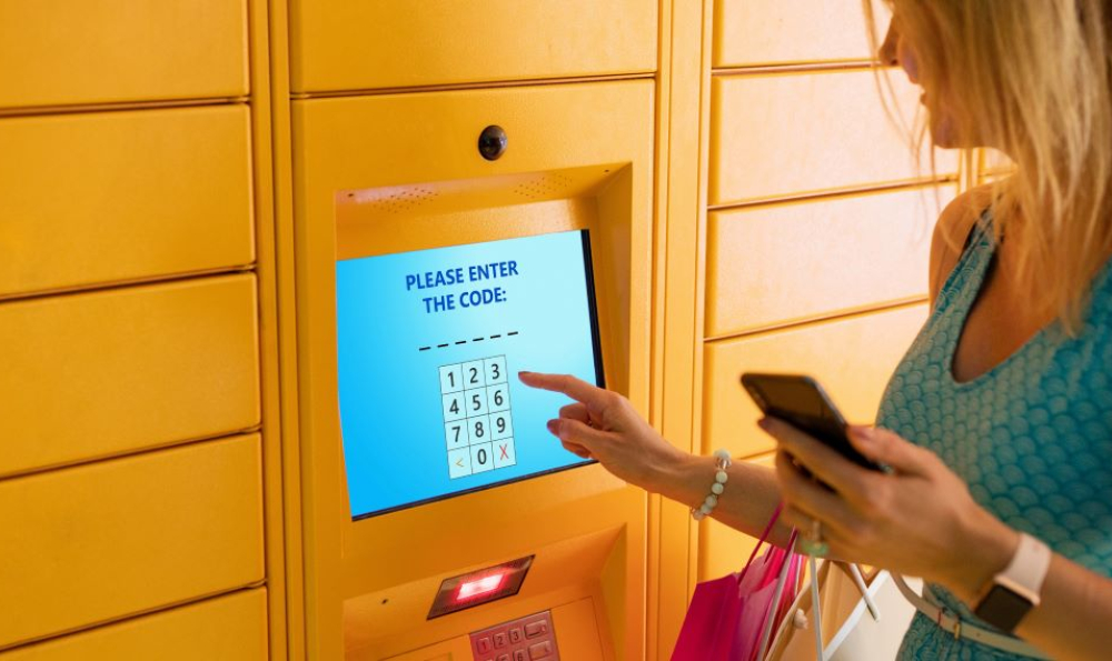 Woman keys in code on screen display on a unit of yellow lockers