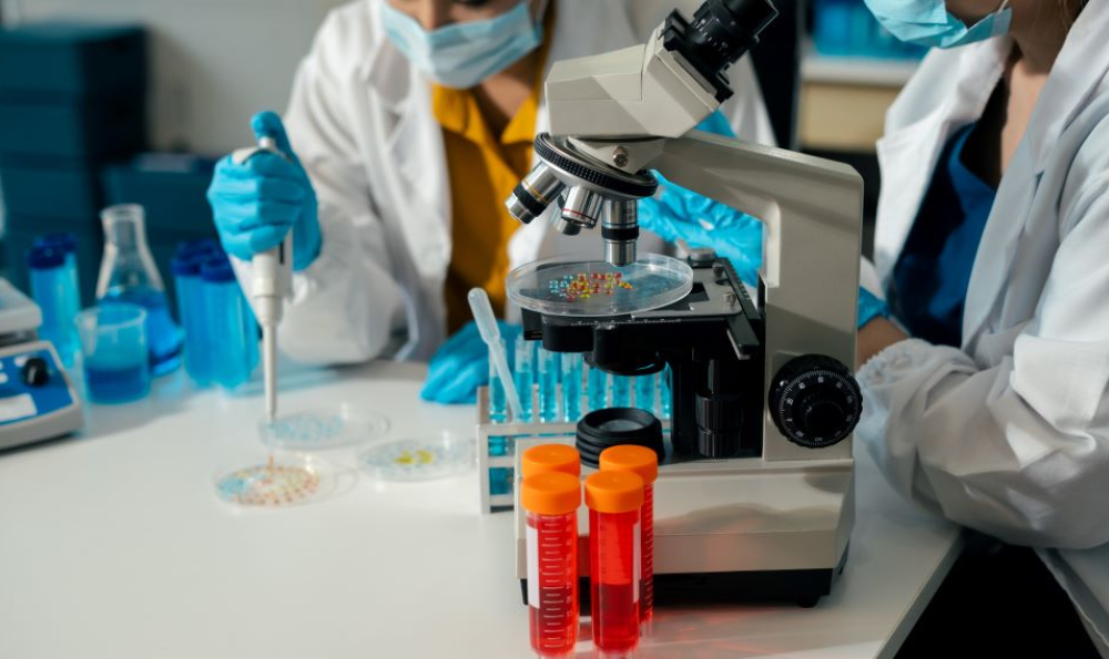 Two masked people in lab coats work with microscopes and other scientific equipment