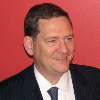 Headshot of Thomas Lily in a black blazer, white shirt and navy tie